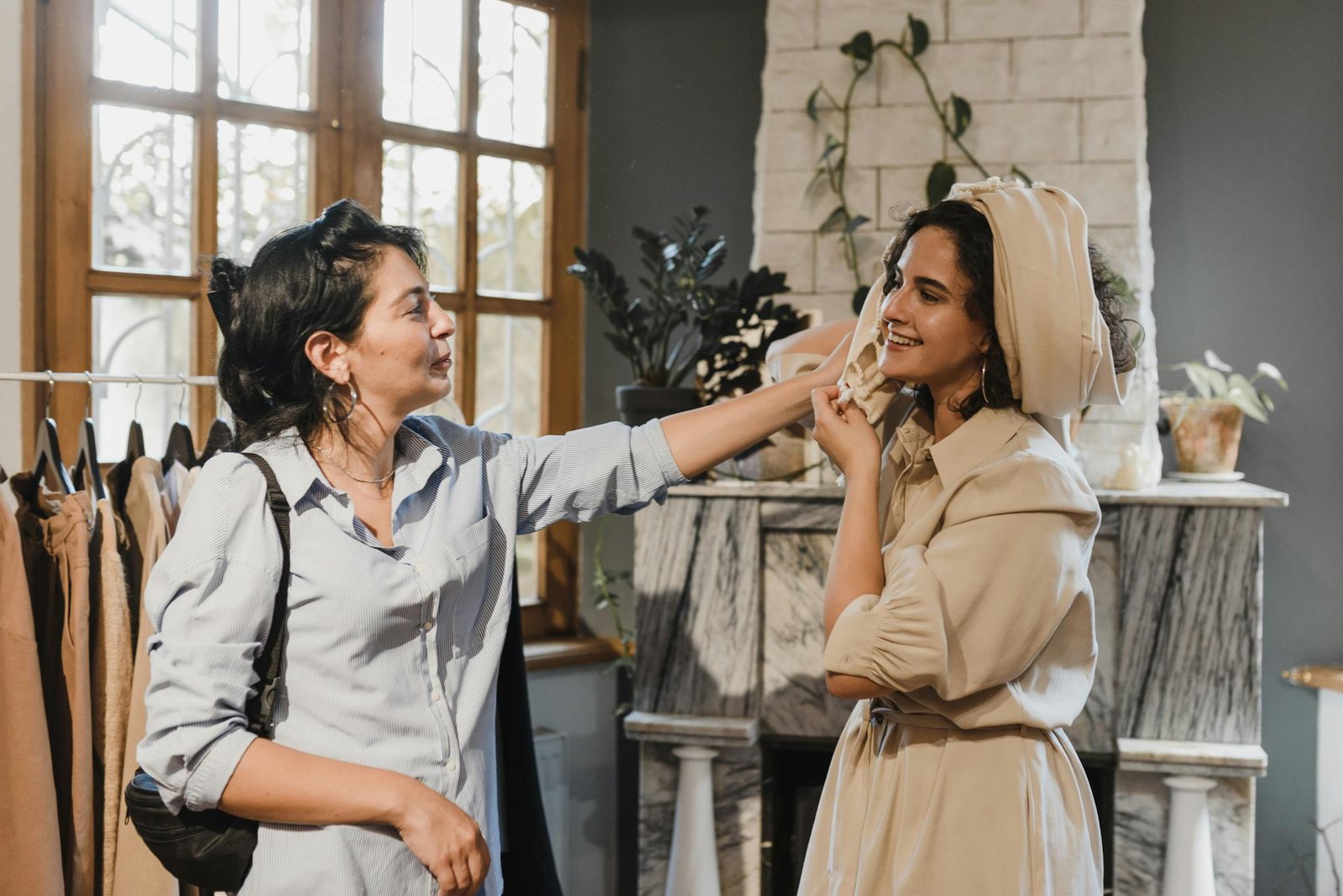 Two women smiling and trying on clothes in an elegant indoor boutique setting.