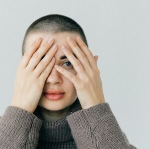 Close-up portrait of a woman with a pensive look, wearing a knitted sweater and covering her face with hands.